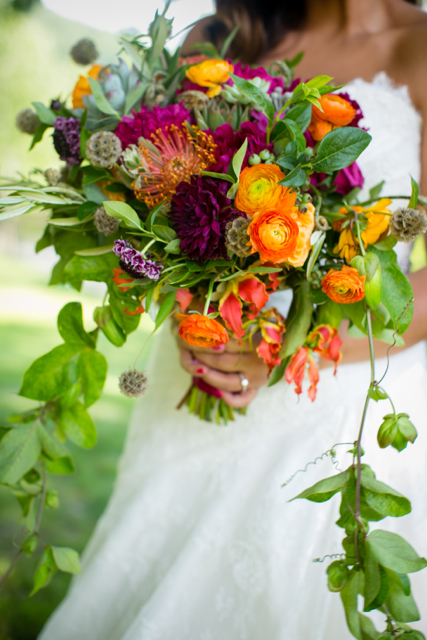 Cascading bridal bouquet by designer Jeanette Kleitz of True Florette - Orangeburg, New York, with orange pincushion protea, orange ranunculus, gloriosa lilies, plum dahlias, scabiosa, scabiosa pods, succulents and passion flower vine