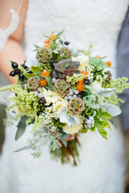 Bridal bouquet by designer Katie Pollard of Color My World Flowers - Nashville, Tennessee, with succulents, scabiosa pods, orange gompherna, wax flower, brunia, scented geranium, cream stock and seeded eucalyptus